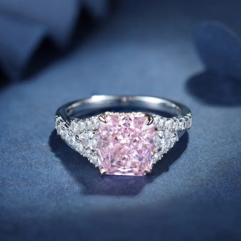 Engagement ring featuring a square-cut pink diamond center stone flanked by smaller white diamonds on the band.