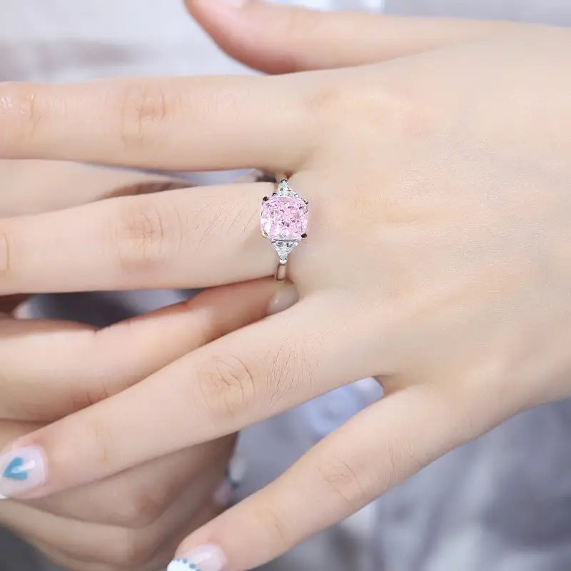 Pink heart-shaped diamond ring on a finger.