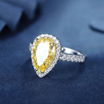 Load image into Gallery viewer, Pear-shaped yellow gemstone ring with diamond halo and band.
