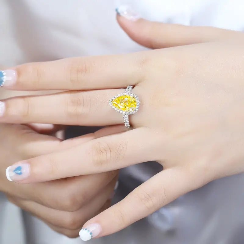 Yellow diamond ring with a halo of smaller diamonds set in a white metal band.