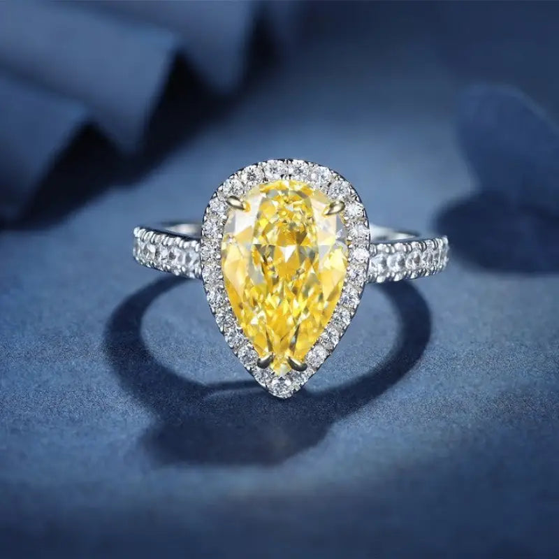 Pear-shaped yellow diamond ring with a halo of smaller white diamonds set in a silver or white gold band.