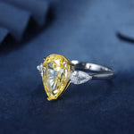 Load image into Gallery viewer, Pear-shaped yellow diamond ring with side accent stones set in a silver or white gold band.
