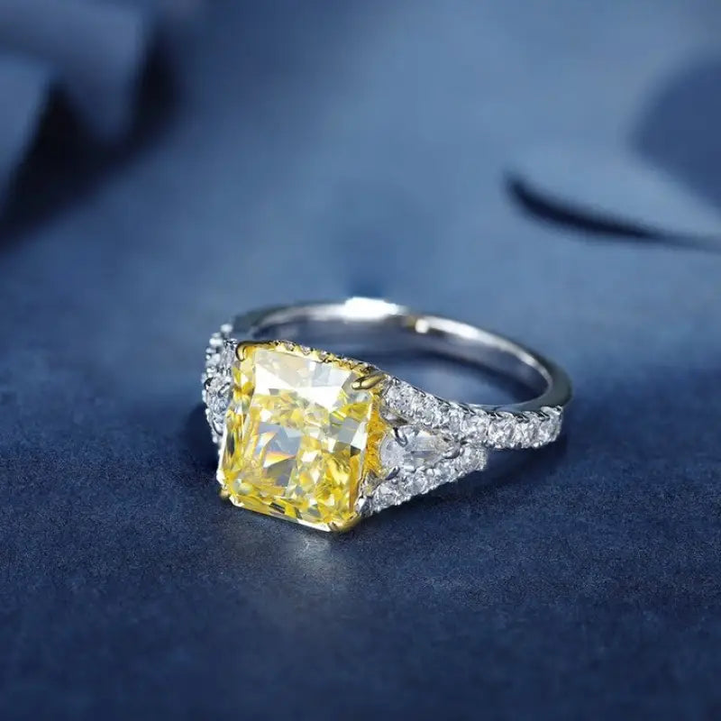 Engagement ring featuring a square-cut yellow diamond center stone flanked by smaller white diamonds on a split shank.