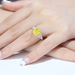 Load image into Gallery viewer, Yellow diamond ring with white diamond accents on a person’s hand.
