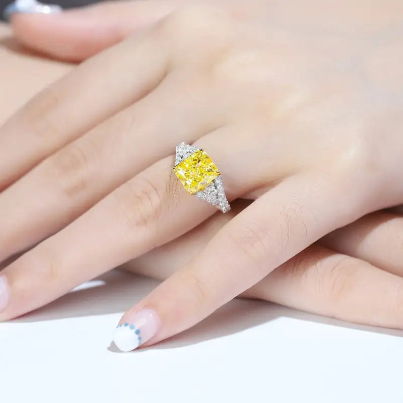 Yellow diamond ring with white diamond accents on a person’s hand.