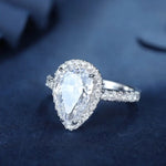 Load image into Gallery viewer, Pear-shaped diamond engagement ring with a halo of smaller diamonds on a silver band.
