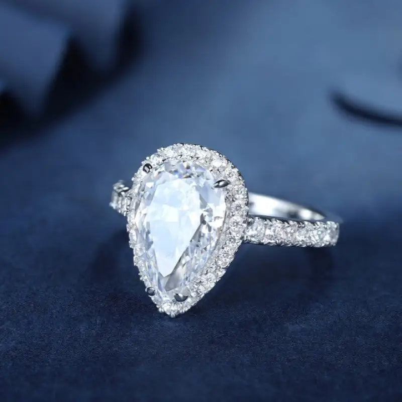 Pear-shaped diamond engagement ring with a halo of smaller diamonds on a silver band.