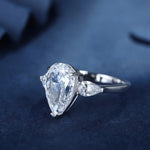 Load image into Gallery viewer, Pear-shaped diamond engagement ring with side stones set in a white metal band.
