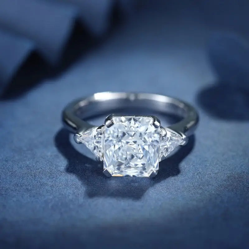 Diamond engagement ring with a radiant-cut center stone flanked by two triangular side diamonds.