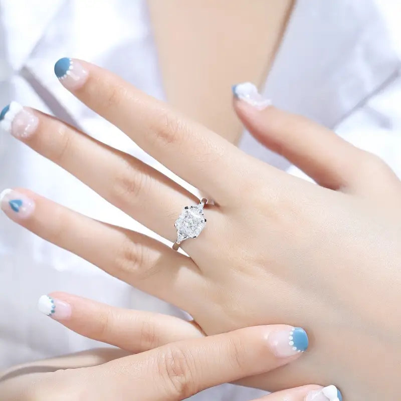 Diamond engagement ring on a woman’s hand with blue-tipped manicure.