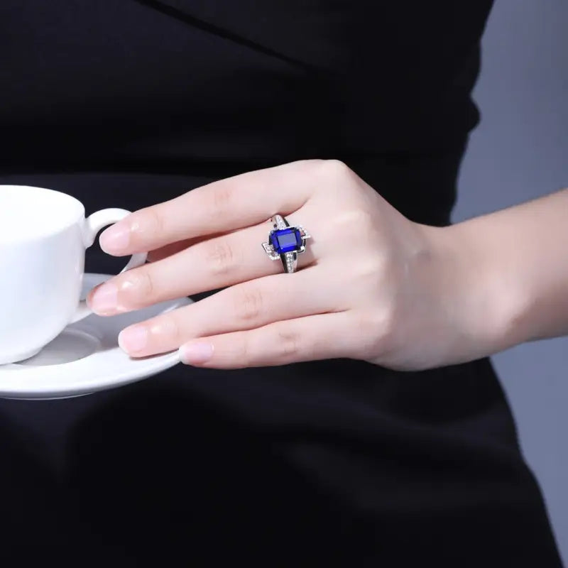 Sapphire ring with diamond accents on a hand holding a white cup.