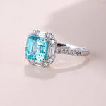 Load image into Gallery viewer, Elegant engagement ring featuring a square-cut aquamarine gemstone surrounded by diamonds in a white gold or platinum setting.
