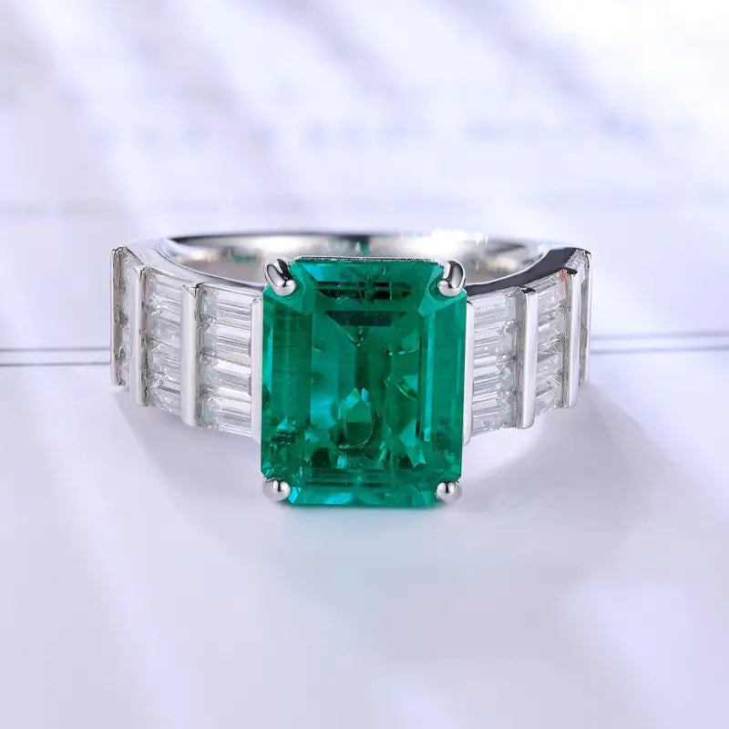 Emerald-cut green gemstone ring with baguette diamond side stones set in a silver or white gold band.