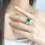 Load image into Gallery viewer, Emerald-cut green gemstone ring with diamond accents on a silver or white gold band.
