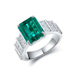 Load image into Gallery viewer, Silver ring featuring a prominent emerald-cut green gemstone flanked by baguette diamonds.
