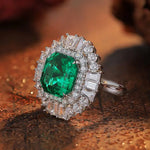 Load image into Gallery viewer, Ornate ring featuring a vibrant emerald-cut green gemstone surrounded by diamonds.
