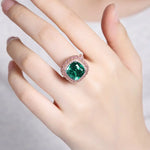 Load image into Gallery viewer, Ornate ring featuring a cushion-cut emerald surrounded by diamonds.
