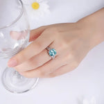 Load image into Gallery viewer, Sparkling blue gemstone ring on a hand next to a wine glass.
