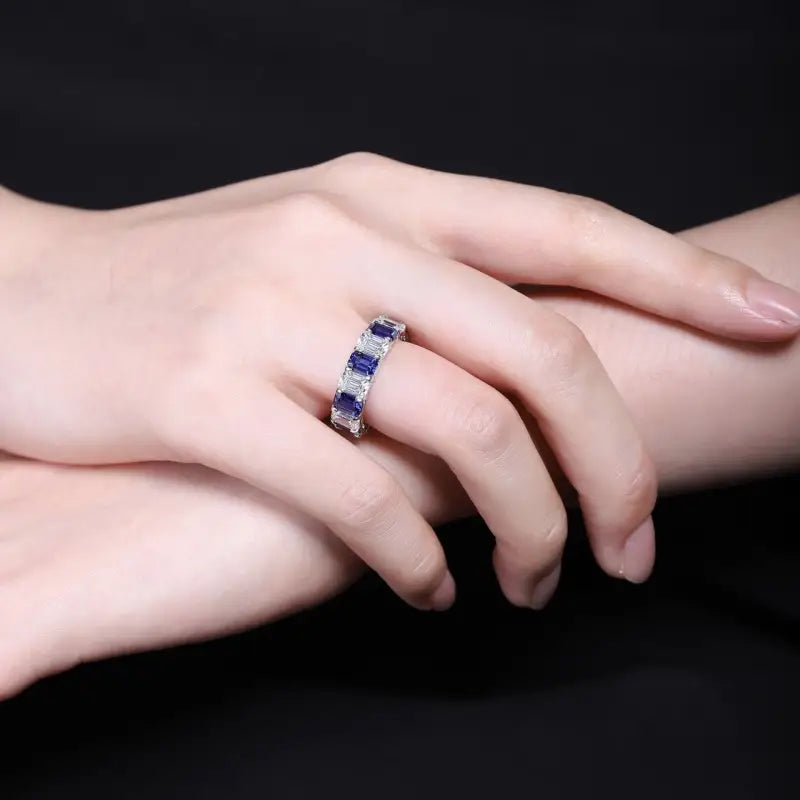 Gemstone ring with alternating blue and purple stones on a pale hand.