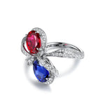 Load image into Gallery viewer, Elegant ring featuring two teardrop-shaped gemstones, one red and one blue, surrounded by small diamonds.
