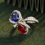 Load image into Gallery viewer, Ornate ring featuring a blue sapphire and red ruby connected by a diamond-encrusted bow design.
