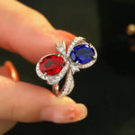 Load image into Gallery viewer, Ornate ring featuring two large gemstones, one red and one blue, set in a diamond-encrusted band.
