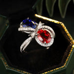 Load image into Gallery viewer, Ornate ring featuring two vibrant gemstones, one red and one blue, set in a diamond-accented precious metal design.
