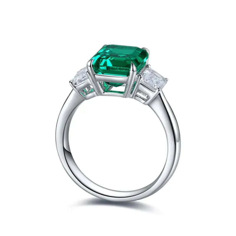 Emerald-cut green gemstone ring with diamond side stones set in white metal.