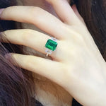 Load image into Gallery viewer, Emerald-cut green gemstone ring with side diamonds on a pale hand.
