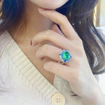 Load image into Gallery viewer, Ornate ring with a vibrant green gemstone surrounded by blue stones.
