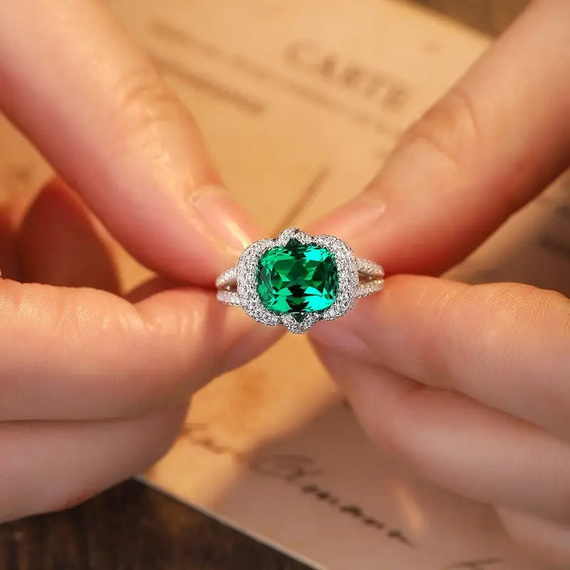 Emerald and diamond ring held between fingers.