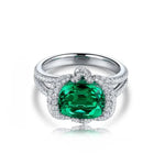 Load image into Gallery viewer, Ornate silver ring featuring a prominent oval-cut emerald surrounded by diamonds.
