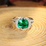 Load image into Gallery viewer, Elegant ring featuring a cushion-cut emerald surrounded by diamonds in a white gold or platinum setting.
