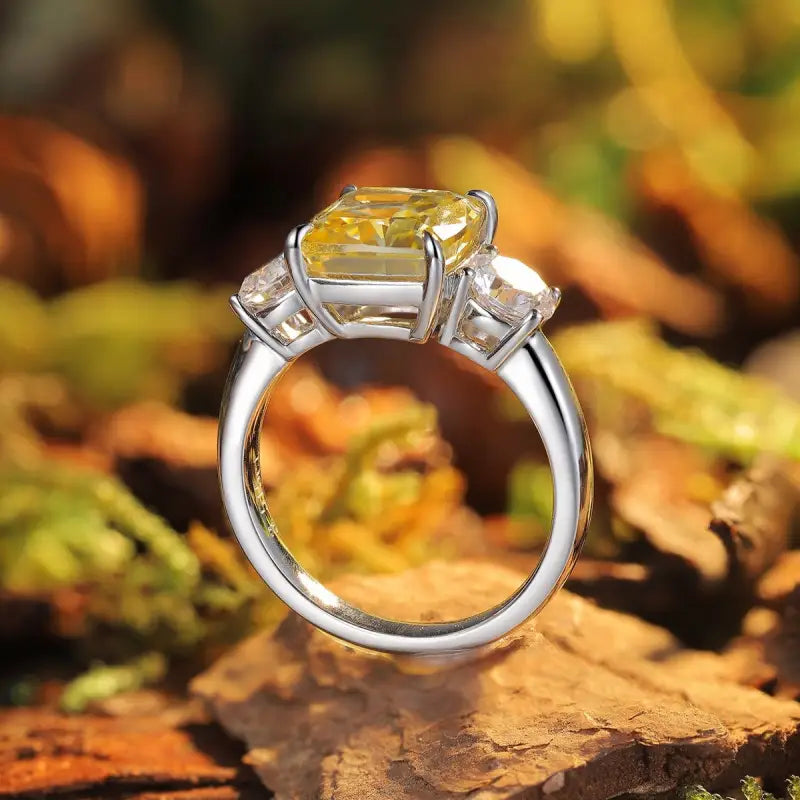 Silver engagement ring with a square yellow diamond center stone and two smaller side diamonds.