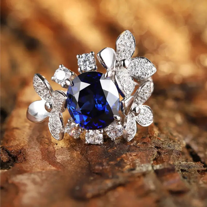 Ornate silver ring featuring a deep blue gemstone surrounded by diamond-encrusted floral designs.