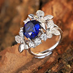 Load image into Gallery viewer, Ornate silver ring featuring a deep blue gemstone surrounded by floral-inspired diamond accents.
