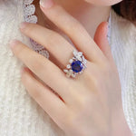 Load image into Gallery viewer, Ornate ring featuring a central blue gemstone surrounded by smaller clear stones.
