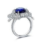 Load image into Gallery viewer, Ornate silver ring featuring a prominent oval blue gemstone surrounded by diamond accents and floral designs.
