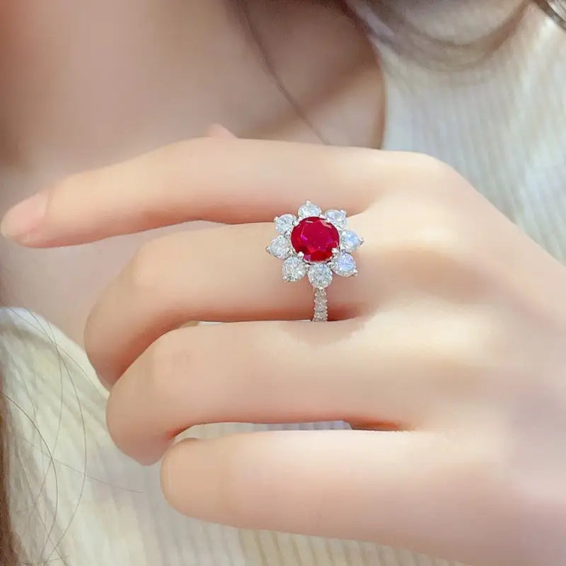 Ruby and diamond floral-style ring on a finger.