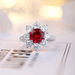 Load image into Gallery viewer, Ornate ring featuring a central red gemstone surrounded by clear diamonds in a floral-like setting.
