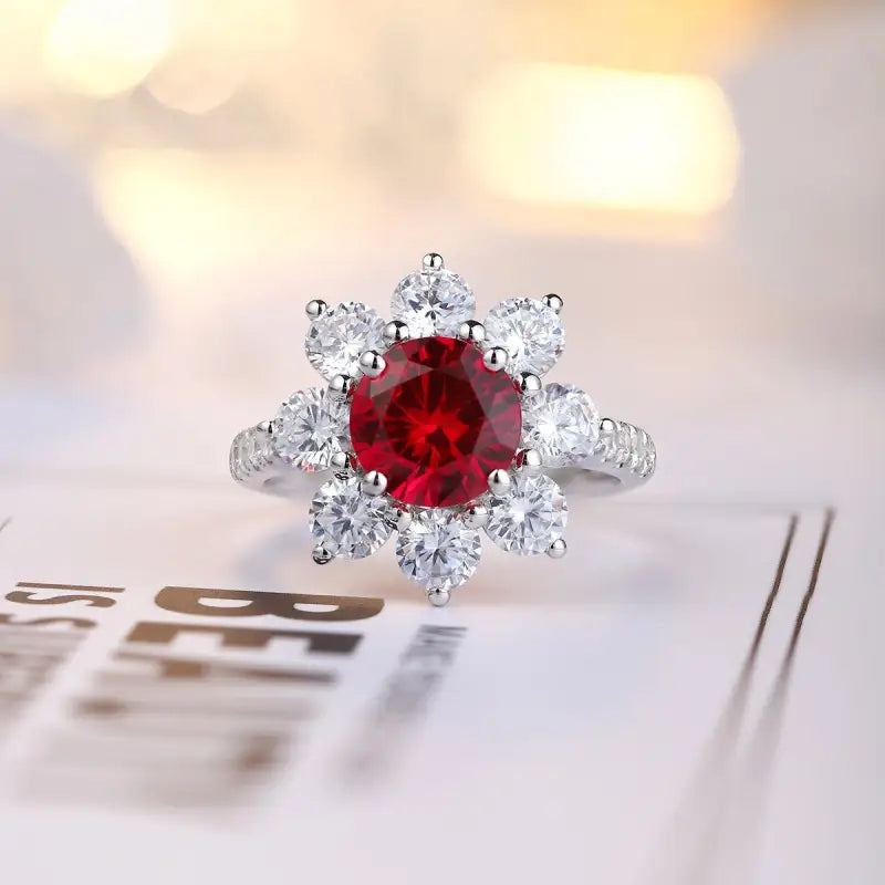 Ornate ring featuring a central red gemstone surrounded by clear diamonds in a floral-like setting.