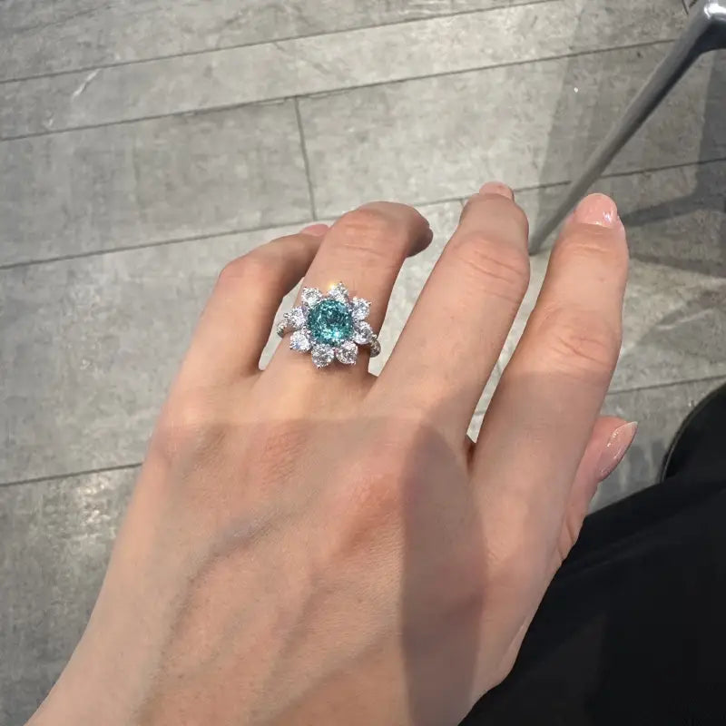 Ornate ring featuring a central blue-green gemstone surrounded by smaller white stones.