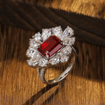 Load image into Gallery viewer, Ornate ring featuring a central rectangular red gemstone surrounded by clear diamonds in a floral-like setting.
