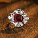 Load image into Gallery viewer, Ornate ring featuring a square-cut red gemstone surrounded by diamond accents.
