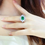 Load image into Gallery viewer, Ornate ring featuring a central emerald-cut green gemstone surrounded by smaller white gemstones.
