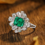 Load image into Gallery viewer, Ornate ring featuring a square emerald surrounded by diamond petals in a floral design.
