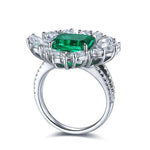 Load image into Gallery viewer, Ornate silver ring featuring a central emerald-cut green gemstone surrounded by clear diamonds.
