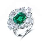 Load image into Gallery viewer, Ornate silver ring featuring a central emerald-cut emerald surrounded by pear-shaped diamonds.
