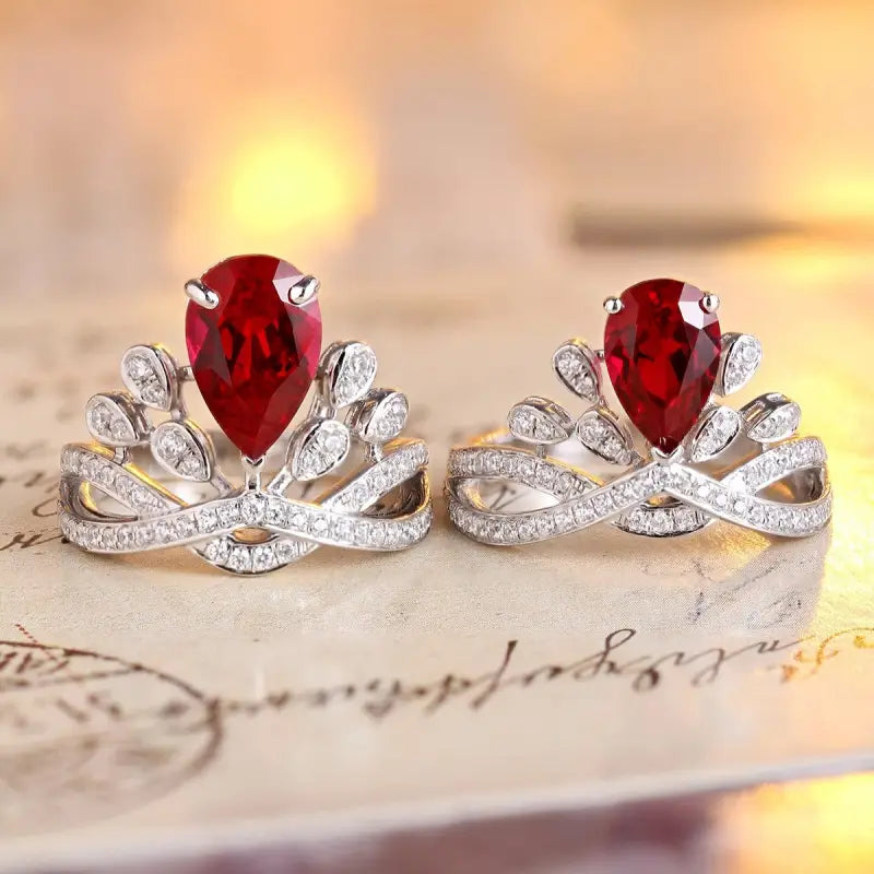 Pair of silver rings with teardrop-shaped red gemstones and diamond accents.