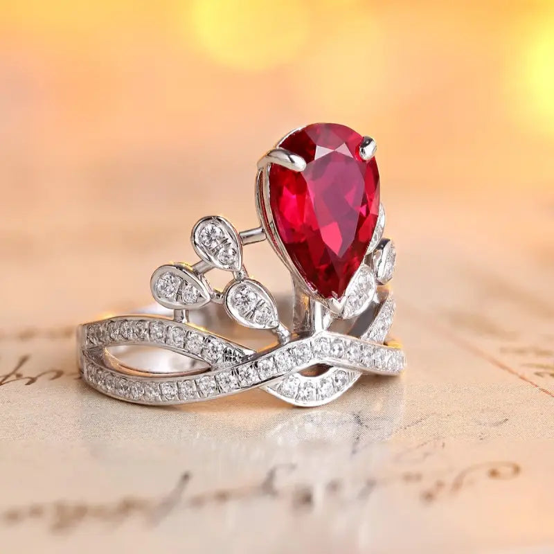 Ornate silver ring featuring a teardrop-shaped red gemstone and diamond accents in a floral design.